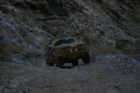 1986 Ford Bronco - A modified SUV navigates a challenging, rocky terrain in a desert landscape.