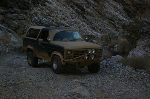 1986 Ford Bronco - A dusty Ford Bronco navigates a rocky, mountainous landscape.