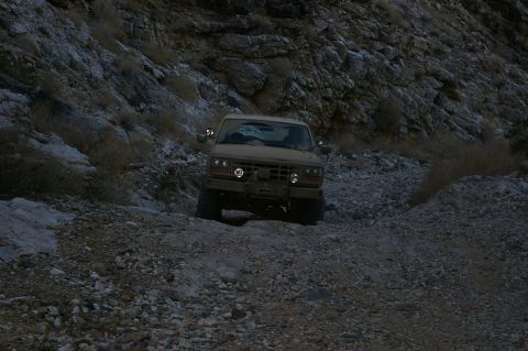 1986 Ford Bronco - A 1986 Ford Bronco navigates a challenging, rocky off-road path in a desert landscape.