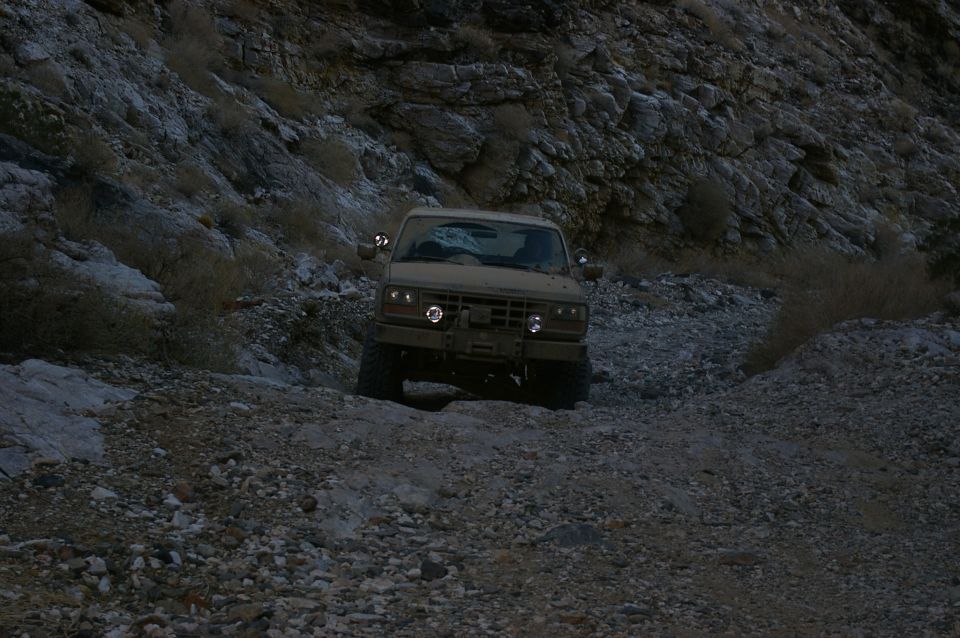 Tan 1986 Ford Bronco driving on a rocky trail, front view