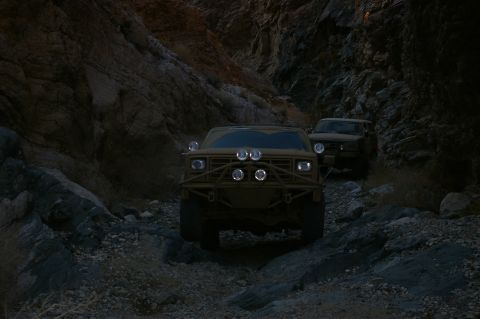 1986 Ford Bronco - Two tan SUVs navigate a rocky canyon trail in low light conditions.