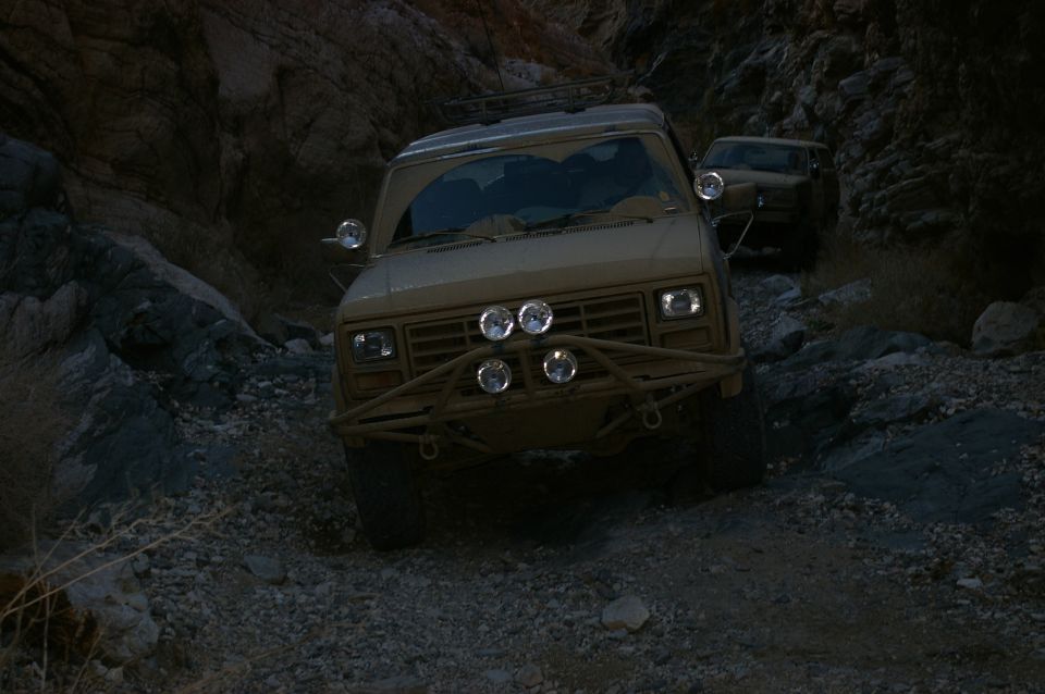 Tan off-road SUV with brush guard and auxiliary lights driving on a rocky trail