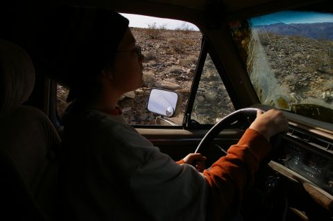 1986 Ford Bronco - A person drives an older vehicle through a desolate, rocky landscape, with a cracked windshield showing the terrain.