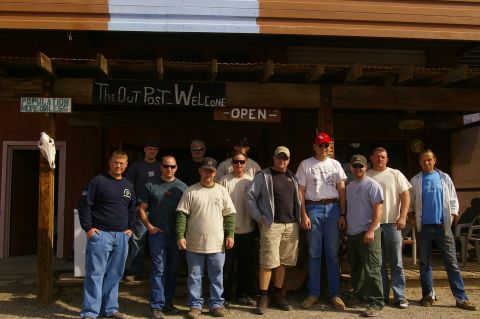 1986 Ford Bronco - A group of men pose for a photo outside a rustic building with a sign that reads 'The Out Post - Welcome'.