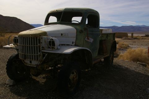 1986 Ford Bronco - An abandoned green and white truck sits in a desolate desert environment under a cloudy sky.