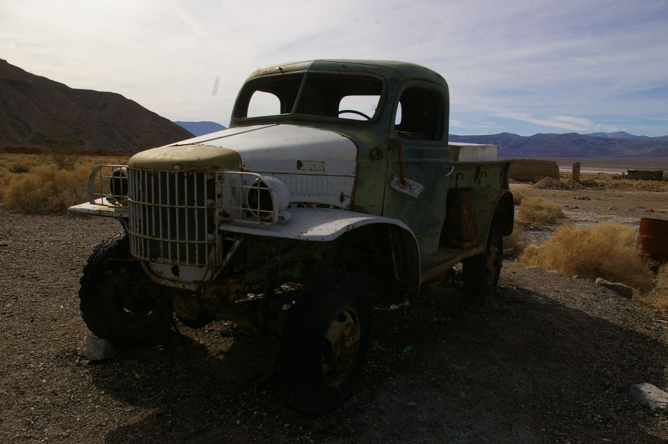 Old green and white truck parked in a dry, desert landscape with mountains in the background