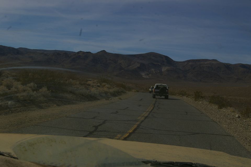 White SUV driving on a desert road with mountains in background