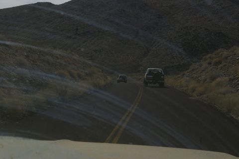 1986 Ford Bronco - Two SUVs travel on a desolate road through a mountainous, arid region.