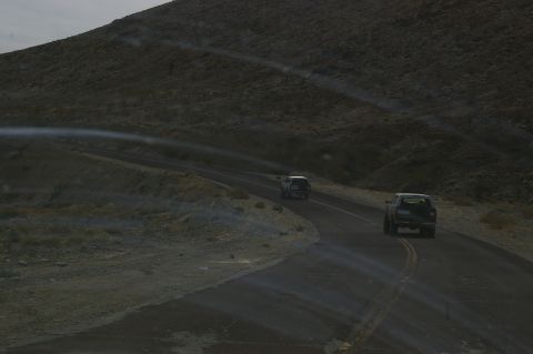1986 Ford Bronco - Two SUVs travel along a winding road in a desolate, mountainous area.