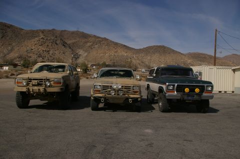 1986 Ford Bronco - Three SUVs are lined up in a desert landscape under a clear blue sky.
