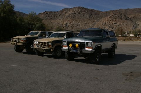 1986 Ford Bronco - Three SUVs are parked in a desert landscape under a bright blue sky.