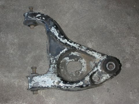 1998 Ford Crown Victoria - cast rear lower control arm with chipped paint and a press-in bushing, lying on a concrete floor.