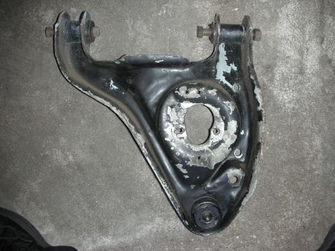 1998 Ford Crown Victoria - black-painted stamped-steel suspension control arm with mounting bushings and a ball joint, lying on a concrete garage floor.