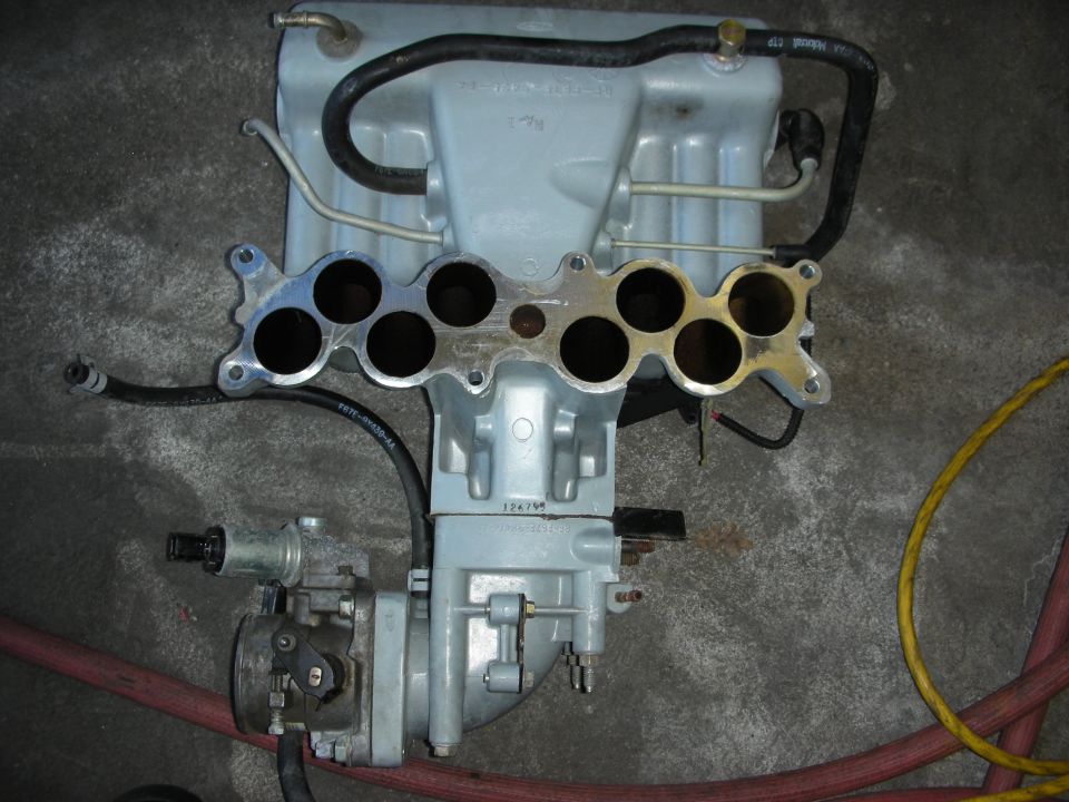Grey aluminum intake manifold with open runner ports and throttle body
