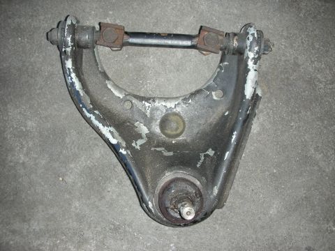 1998 Ford Crown Victoria - weathered suspension control arm with peeling paint, a center ball joint and a rusted pivot shaft, on concrete.