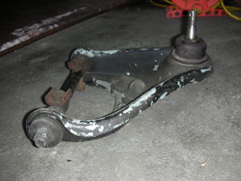 1998 Ford Crown Victoria - suspension control arm with two ball joints and chipped black paint resting on a concrete floor near a red jack.