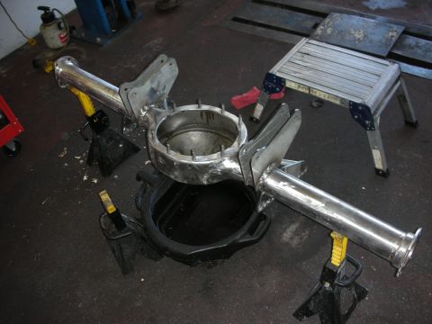 1998 Ford Crown Victoria - Polished tubular rear-axle housing components mounted on yellow jack stands in a workshop, with a step stool nearby.