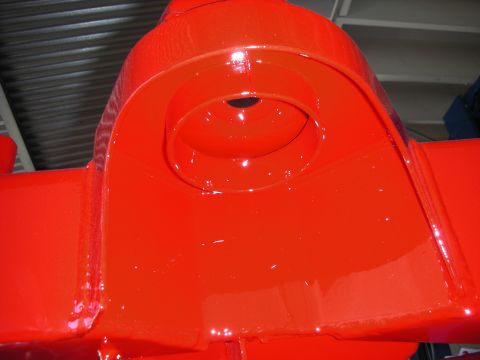 1998 Ford Crown Victoria - Close-up of a freshly glossy red-painted vehicle frame bracket with a cupped recess and center hole.