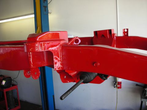 1998 Ford Crown Victoria - glossy red-painted vehicle frame rail and crossmember section raised on a shop lift, with a steering tie rod visible.