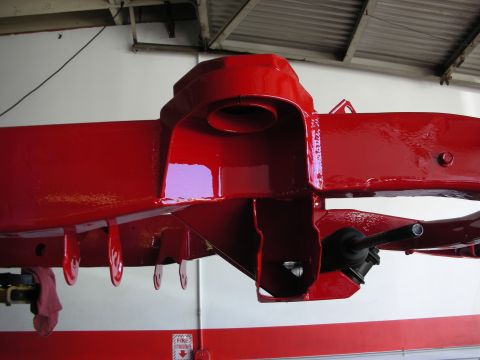 1998 Ford Crown Victoria - glossy red-painted frame crossmember with a cupped bracket and brake hardware, viewed from below on a shop lift.