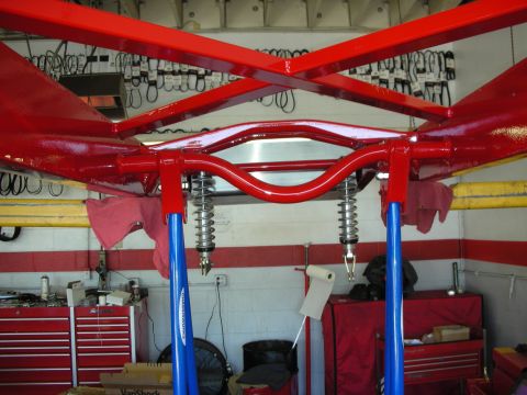 1998 Ford Crown Victoria - glossy red-painted X-member chassis fitted with coilover shocks, raised on blue two-post lift arms in a busy garage.