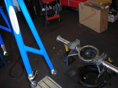 1998 Ford Crown Victoria - Blue powder-coated tubular suspension arms beside polished axle housing components on a garage floor near a parts box.