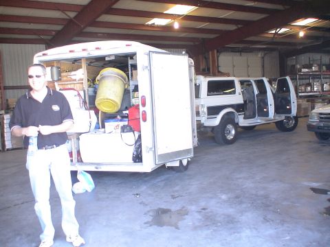 1993 Ford C-350 (Centurion Conversions) - A white van with black trim and open doors is parked inside a warehouse next to a trailer.