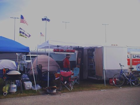 1993 Ford C-350 (Centurion Conversions) - A campsite is set up with tents, a trailer, and a bicycle, with American flags in the background.