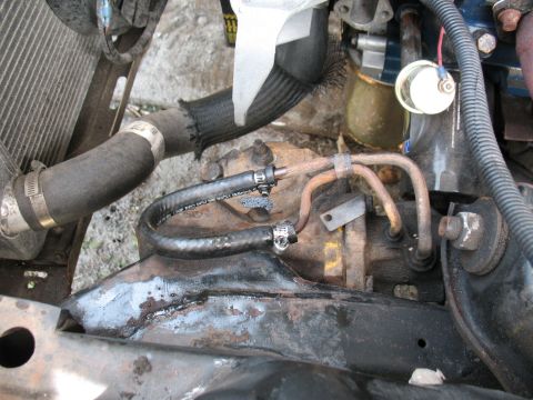 1985 Ford Crown Victoria LTD - Close-up view of engine components, including hoses and metal tubing, with visible rust on the frame.