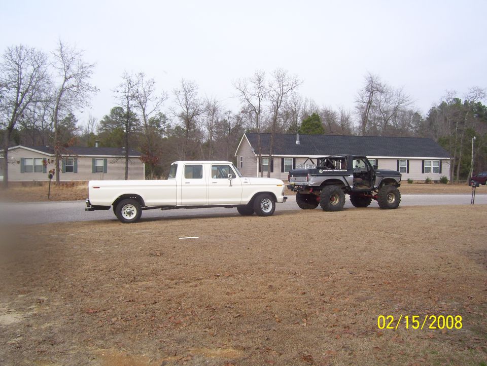 White crew cab truck towing a lifted black Bronco, side view