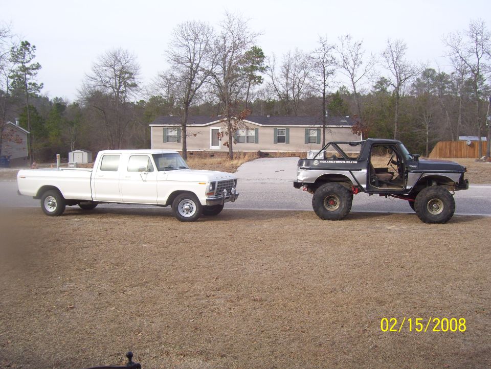 Lifted Bronco-like vehicle and white crew cab pickup truck parked side-by-side