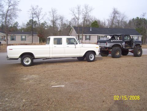 1978 Ford Bronco - Two Ford trucks are parked side-by-side on a dirt lot with houses in the background.