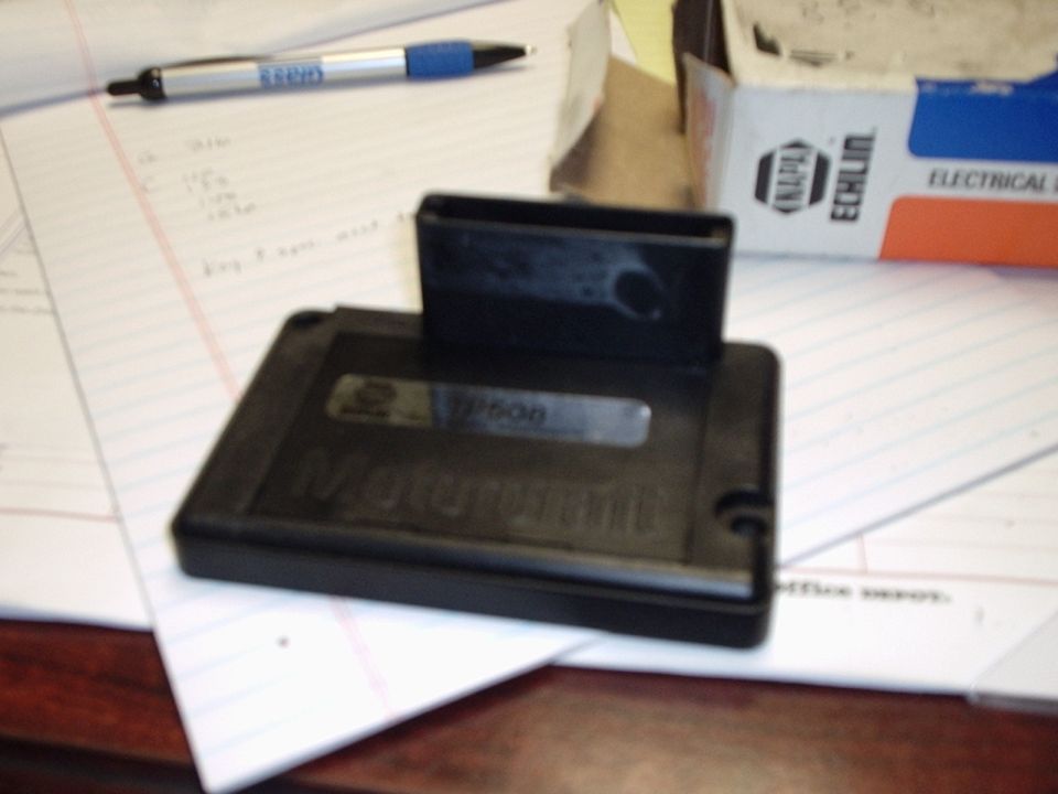 Black electronic control module labeled "Motorcraft P608" with a connector attached, resting on papers