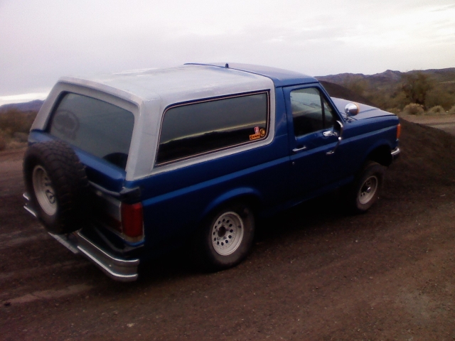 Blue Ford Bronco with a white top, spare tire on the back, chrome bumper, and aftermarket wheels