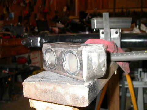 1990 Ford Bronco - A fabricated metal component with dual apertures is secured on a wooden support within a cluttered garage setting.