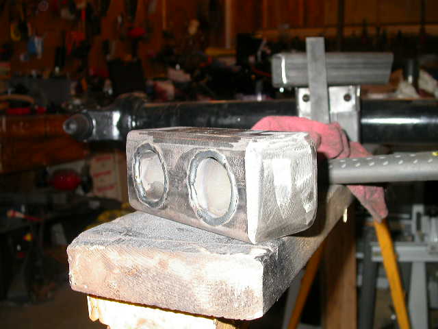 metal block with two circular openings, resting on wood, in a workshop