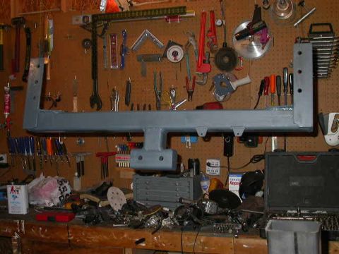 1990 Ford Bronco - A metal frame part is displayed in a workshop setting, surrounded by various tools and equipment.