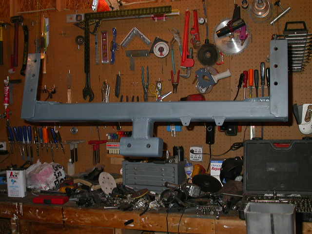Gray metal frame part hanging above a workbench with tools and parts