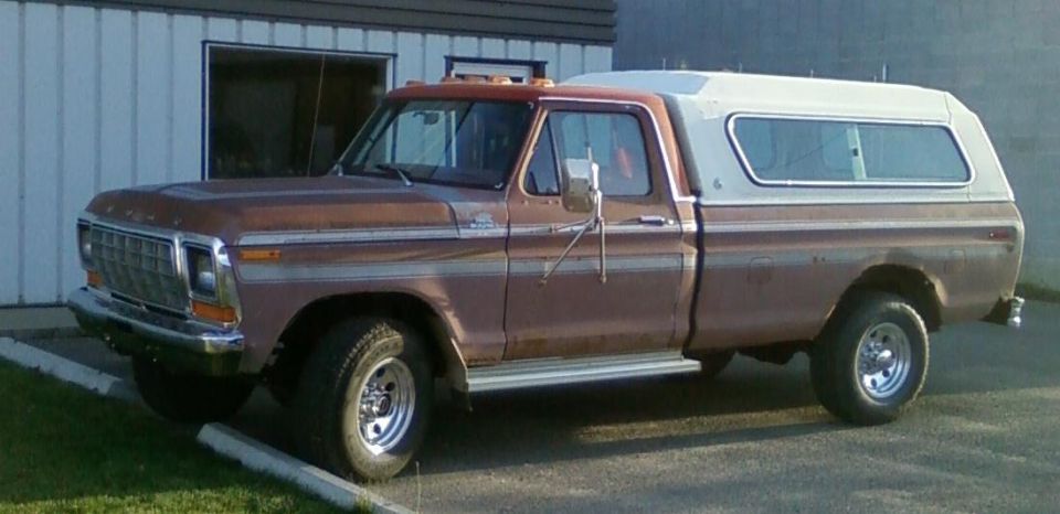 Brown Ford pickup truck with a white camper shell, parked outside a building