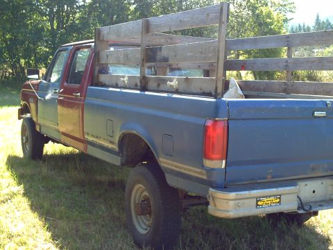 1991 Ford F-350 - This truck has a blue bed and rear, but a red driver's side door and fender. It has a wooden rack in the bed.