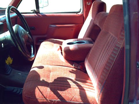 1991 Ford F-350 - The interior of a 1991 Ford F-350 truck features red cloth upholstery and a center console with cup holders.