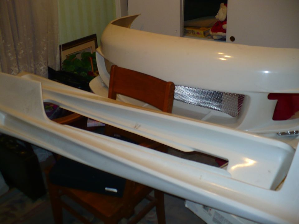 White car body kit parts, including a front bumper and side skirts, are laid out indoors