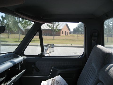 1981 Ford Bronco - View from inside a truck cab, looking out at a brick building and trees.