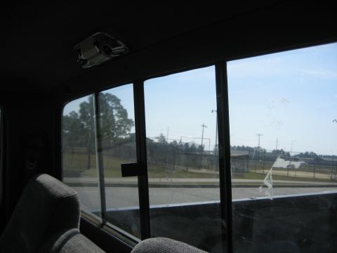 1981 Ford Bronco - View from the interior of a vehicle, looking out the rear window at a fence and trees under a clear sky.