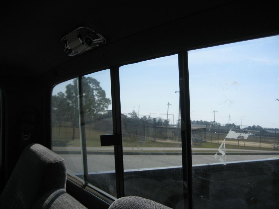 Interior view from rear seat looking out, showing a cracked window and a distant fence