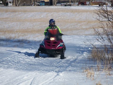1996 Arctic Cat Puma - Rider on a snowmobile travels down a groomed trail in a winter landscape.