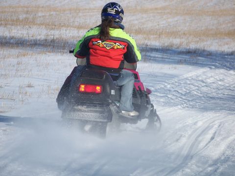 1996 Arctic Cat Puma - A rider on a 1996 Arctic Cat Puma snowmobile kicks up snow as they travel across a winter field.