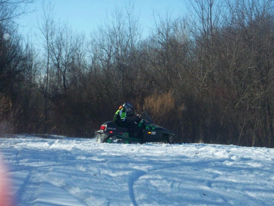 Green and black Arctic Cat snowmobile with rider on snowy field