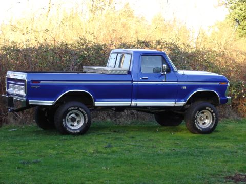 1973 Ford F-250 - A blue 1973 Ford F-250 pickup truck is shown from the side, parked on a grassy area with trees in the background.