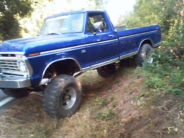 Lifted blue Ford single-cab pickup with large off-road tires on a dirt trail